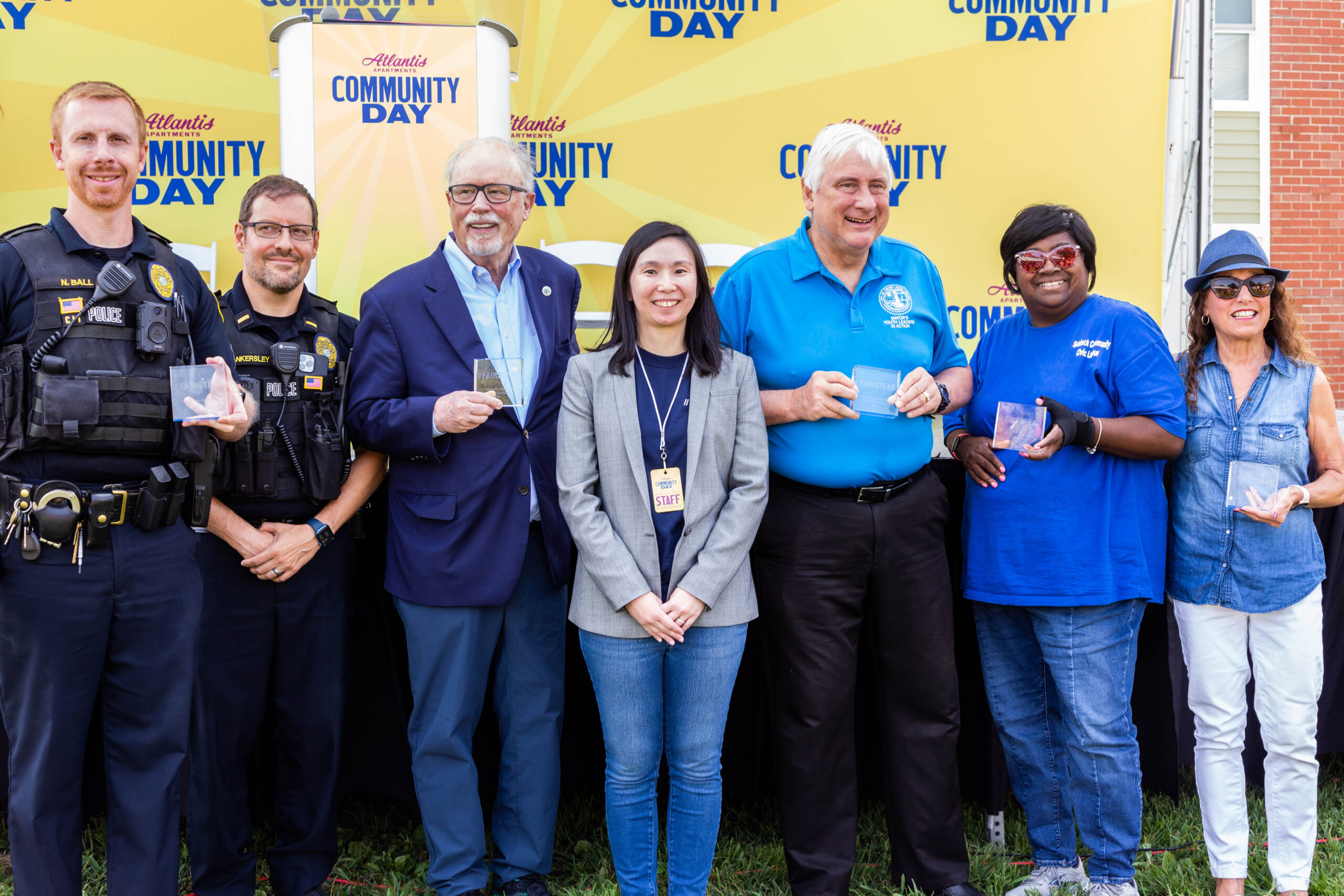 police officers, elected officials, fairstead staff, and community members smiling in front of an Atlantis community day banner