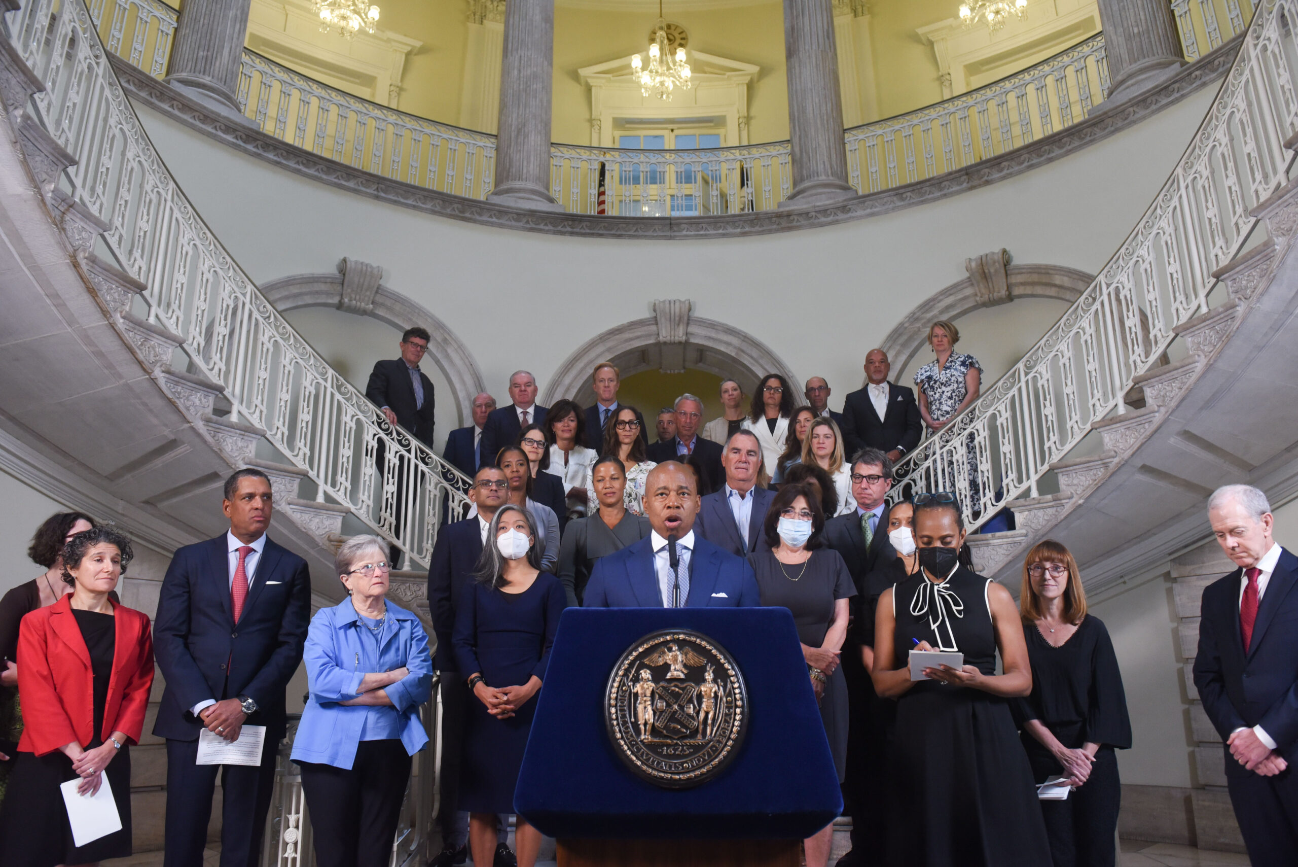 Mayor of New York standing behind podium with group of people behind him